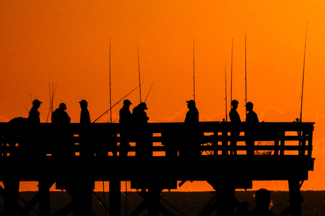 A group of fishermen silhouetted by the sunrise over the Atlantic Ocean gather to try their luck on Front Beach fishing pier in South Carolina on October 16, 2025. (Photo by Richard Ellis/ZUMA Press Wire/Rex Features/Shutterstock)