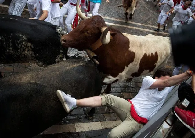 Participants run next to a Puerto de San Lorenzo's fighting bull on the first day of the San Fermin bull run festival in Pamplona, northern Spain on July 7, 2018. Each day at 8am hundreds of people race with six bulls, charging along a winding, 848.6-metre (more than half a mile) course through narrow streets to the city's bull ring, where the animals are killed in a bullfight or corrida, during this festival dating back to medieval times and also featuring religious processions, folk dancing, concerts and round-the-clock drinking. (Photo by Jaime Reina/AFP Photo)