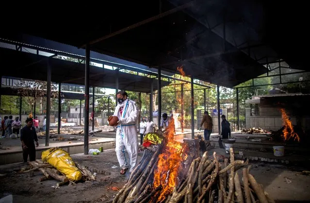 A man performs the last rites to his wife who died of the Covid-19 coronavirus disease during a mass cremation at a crematorium on April 20, 2021 in New Delhi, India. Covid-19 cases are spiralling out of control in India, with daily infections approaching 300,000, according to health ministry data, bringing the nationwide tally of infections to almost 14 million. The latest wave has already overwhelmed hospitals and crematoriums. (Photo by Anindito Mukherjee/Getty Images)