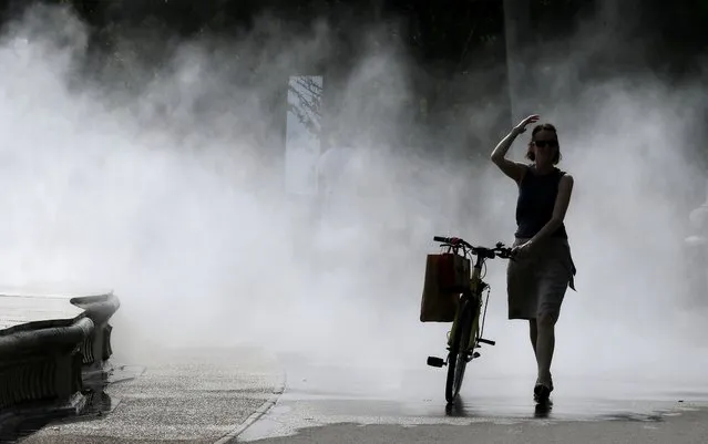 A woman gets cooled off while passing a water mist during a hot summer day in Bucharest, Romania, 24 July 2023. Meteorologists are forecasting above-normal temperatures in Romania's capital and southern regions for the next two days. Bucharest is being announced for tomorrow with the red code alert because of air temperatures above 40 Celsius degrees in the shade. (Photo by Robert Ghement/EPA/EFE)