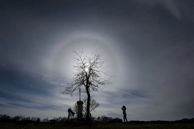 A woman looks at the halo phenomenon around the sun above Salgotarjan, in Hungary, Sunday, March 28, 2021. The halo is an optical phenomenon that appears around the sun or the moon, caused by the light interacting with ice crystals. (Photo by Peter Komka/MTI via AP Photo)