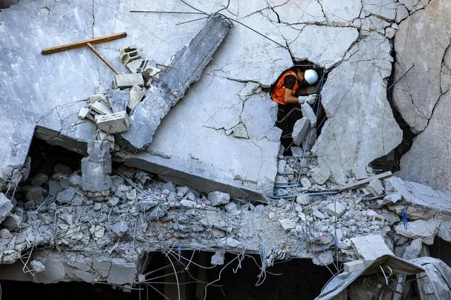 A Palestinian civil defence member stands through a crack in a collapsed building hit by Israeli bombardment while searching for victims and survivors, in Khan Yunis in the southern Gaza Strip on October 19, 2023. Thousands of people, both Israeli and Palestinians have died since October 7, 2023, after Palestinian Hamas militants based in the Gaza Strip, entered southern Israel in a surprise attack leading Israel to declare war on Hamas in Gaza on October 8. (Photo by Mahmud Hams/AFP Photo)