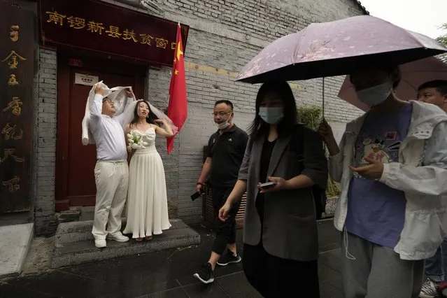 A wedding couple takes shelter from the rain as visitors pass through the popular Nanluoguxiang alley way in Beijing on Saturday, July 3, 2021. (Photo by Ng Han Guan/AP Photo)