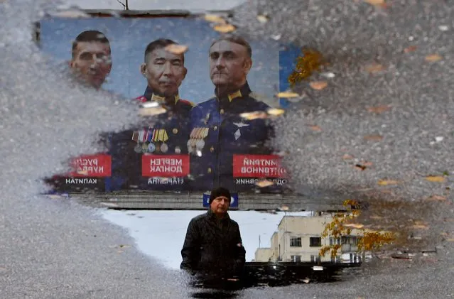 A man walks past a billboard reflecting in a puddle depicting the portraits of Russian Army officers in Saint Petersburg on November 8, 2023. (Photo by Olga Maltseva/AFP Photo)