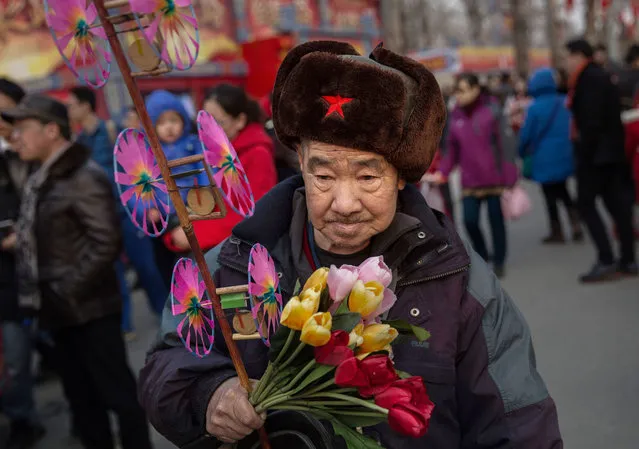 A Chinese man carries a traditional toy and flowers at a local fair during Spring Festival celebrations on February 10, 2016 in Beijing, China. The Chinese Lunar New Year also known as the Spring Festival, which is based on the Lunisolar Chinese calendar, is celebrated from the first day of the first month of the lunar year and ends with Lantern Festival on the fifteenth day. This new year marks the Year of the Monkey. (Photo by Kevin Frayer/Getty Images)