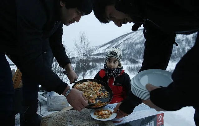 Afghan asylum seeker Roheek Yausofi waits his turn for food cooked on an open fire, with fish caught the day before by his father, on the island of Seiland, northern Norway, Tuesday, February 2, 2016. (Photo by Alastair Grant/AP Photo)