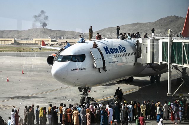 Afghan people climb atop a plane as they wait at the Kabul airport in Kabul on August 16, 2021, after a stunningly swift end to Afghanistan's 20-year war, as thousands of people mobbed the city's airport trying to flee the group's feared hardline brand of Islamist rule. (Photo by Wakil Kohsar/AFP Photo)