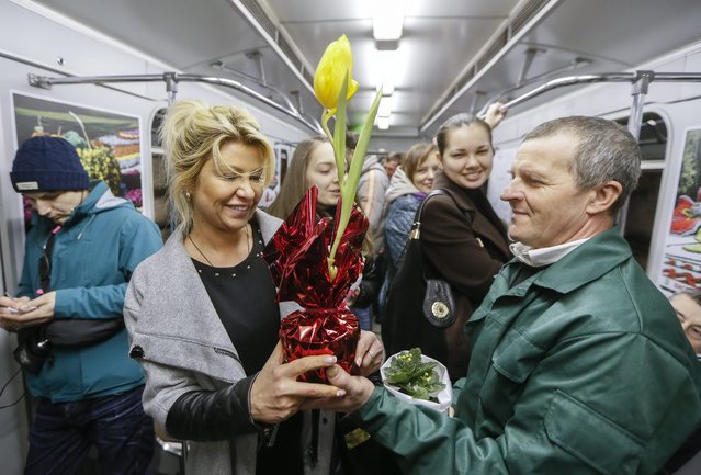 Female metro passengers hold flowers presented to them by metro workers, prior to International Women's Day in Kiev, Ukraine, 02 March 2016. The hustle and bustle of the morning commute is broken up by an unexpected surprise. The first passengers to step on the train receive – a warm welcome and a pot of flowers. One woman says, “It's very nice. All the running around and then you're given a flower, it's not often. It's very nice. I'm going to take care of this flower”. (Photo by Sergey Dolzhenko/EPA)