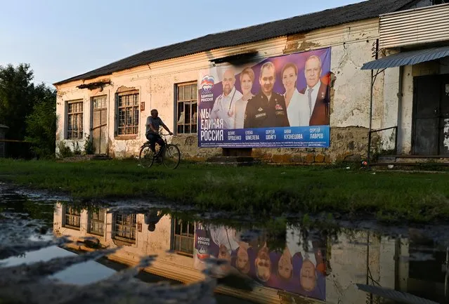 A man rides his bicycle past a campaign poster of the United Russia political party placed on a disused local community center head of the Russian parliamentary and regional voting in the village of Zarevo, the Republic of Adygea, Russia on September 15, 2021. (Photo by Alexey Malgavko/Reuters)
