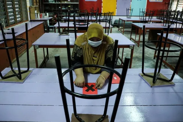 A teacher marks a table as part of social distancing measures at a secondary school, as schools reopen amid the coronavirus disease (COVID-19) outbreak, in Kuala Lumpur, Malaysia on October 4, 2021. (Photo by Lim Huey Teng/Reuters)
