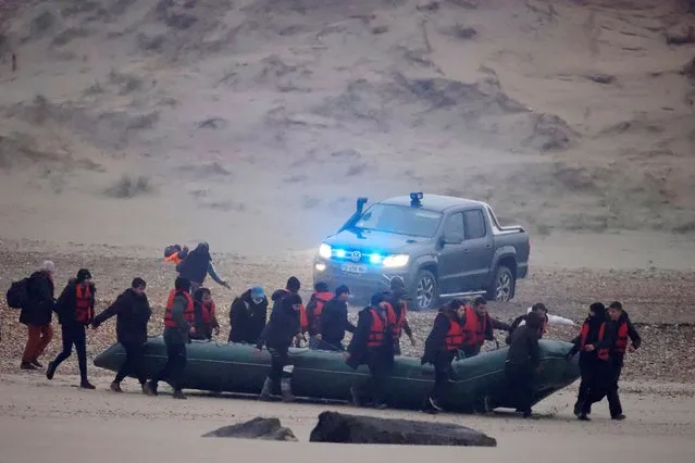 French police stand near as a group of more than 40 migrants run with an inflatable dinghy, to leave the coast of northern France and to cross the English Channel, near Wimereux, France, November 24, 2021. (Photo by Gonzalo Fuentes/Reuters)