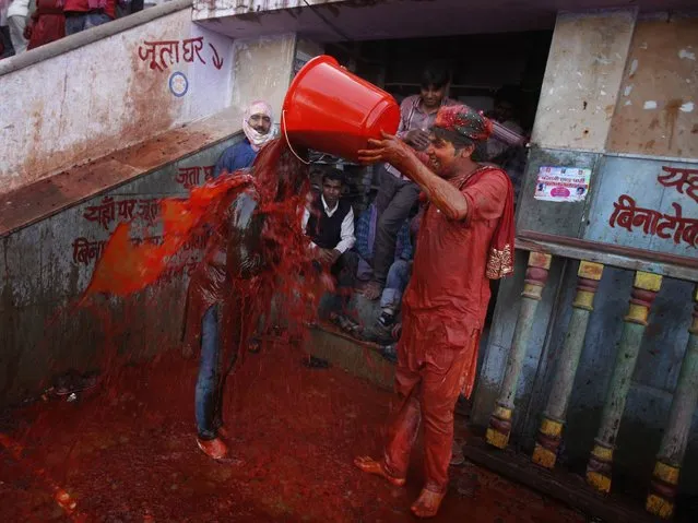 A Hindu man pours a bucket of colored water on a woman outside the Ladali or Radha temple before the procession for the Lathmar Holi festival. (Photo by Altaf Qadri/AP Photo)