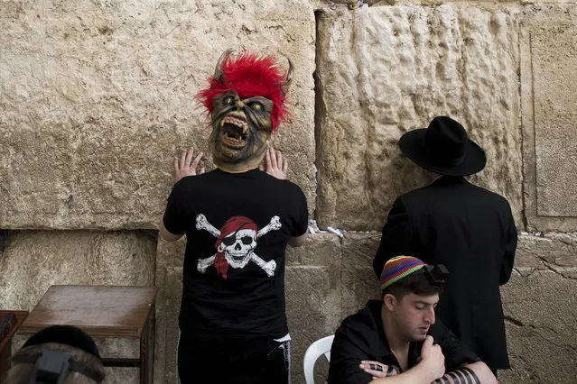 An Israeli  wearing a monster mask prays next to an Ultra Orthodox Jew during the Jewish Holiday of Purim in the Mea Shaarim neighborhood in Jerusalem, Israel, March 17, 2014. The Jewish holiday of Purim celebrates the Jews' salvation from genocide in ancient Persia, as recounted in the Scroll of Esther. (Photo by Abir Sultan/EPA)