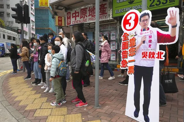 People wait to cross a street next to a cut out of pro-Beijing candidate Ng Chau-pei in Hong Kong Sunday, December 19, 2021. Hong Kong was voting Sunday in the first election since Beijing amended the laws to reduce the number of directly elected lawmakers and vet candidates to ensure that only those loyal to China can run. (Photo by Vincent Yu/AP Photo)