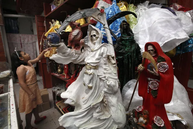 In this February 19, 2017 photo, a child arranges statues of the Death Saint at Mercy Church on the edge of Mexico City's Tepito neighborhood. Saint Death, or “Santa Muerte”, devotees say she has millions followers and various names: the Death Saint, the White Girl, the Skinny One or just Sister. But she doesn't have her own religion, and her followers are Catholics. (Photo by Marco Ugarte/AP Photo)
