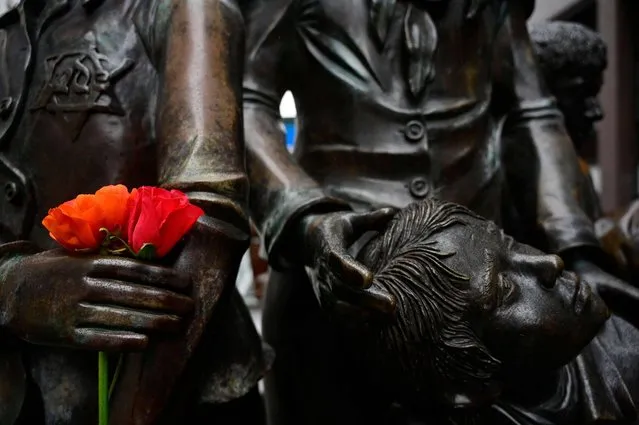 Roses are placed in the hand of one of the statues part of the “Trains to Life – Trains to Death” bronze sculpture at Berlin's Friedrichstrasse street on January 27, 2022, the International Holocaust Remembrance Day. The sculpture is dedicated to Jewish children saved by so-called "Kindertransporte" which brought them to the United Kingdom and other countries, as well as to children brought by trains to the Nazi death camps. Israeli architect and sculptor Frank Meisler, who made the sculpture, was himself evacuated with a children's transport and survived the Holocaust, whereas his parents were killed in Auschwitz. (Photo by John MacDougall/AFP Photo)