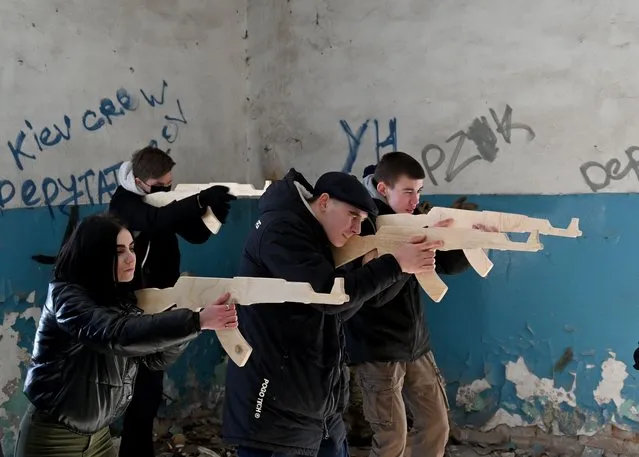 Civilians train to hold wooden replicas of Kalashnikov rifles, as they take part in a training session at an abandoned factory in the Ukrainian capital of Kyiv on February 6, 2022. Amid fears of a potential invasion by Russian troops massed on Ukraine's border, within the framework of the training there were classes on tactics, paramedics, training on the obstacle course. The training is conducted by instructors with combat experience, members of the movement “Total Resistance”. Ukraine's presidency on February 06, insisted the chance of resolving soaring tensions with Russia through diplomacy remained greater than that of an attack, as the US warned Moscow was stepping up preparations for an invasion. “An honest assessment of the situation suggests that the chance of finding a diplomatic solution for de-escalation is still substantially higher than the threat of further escalation”, said presidency advisor Mykhailo Podolyak in a statement. (Photo by Sergei Supinsky/AFP Photo)