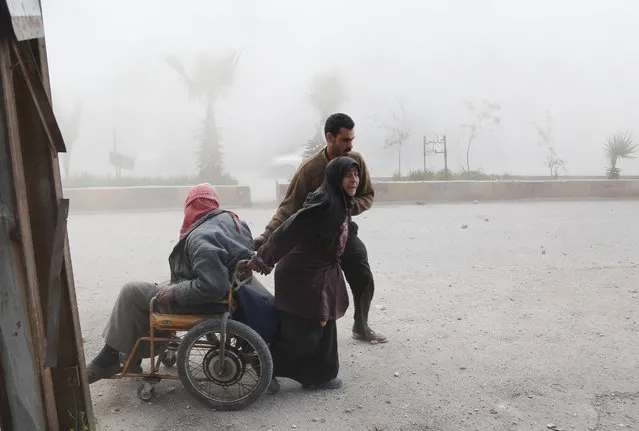 A Syrian woman pulls her husband on a wheelchair as they evacuate from their home following a reported air strike on the rebel-controlled town of Hammuriyeh, in the eastern Ghouta region on the outskirts of the capital Damascus, on March 25, 2017. At least 16 civilians were killed and dozens wounded in an air strike on a rebel-held area outside Damascus, the Syrian Observatory for Human Rights monitor said. (Photo by Abdulmonam Eassa/AFP Photo)