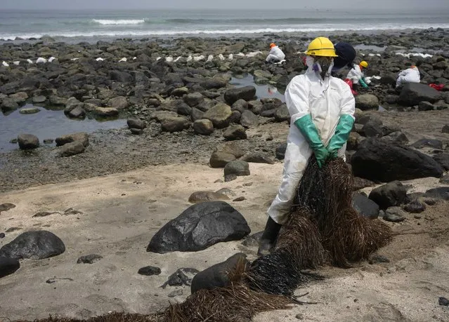 A worker holds a type of skimmer that collects oil waste during a clean-up campaign on Pocitos Beach in Ancon, Peru, Tuesday, February 15, 2022. One month later, workers continue the clean-up on beaches after contamination by a Repsol oil spill. (Photo by Martin Mejia/AP Photo)