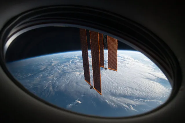 In this view from a window aboard the SpaceX Crew Dragon Endeavour, a pair of the ISS's main solar arrays drape across the Earth's horizon as the orbital lab soars 271 miles above the south Atlantic between Argentina and South Africa on May 20, 2021. (Photo by NASA)