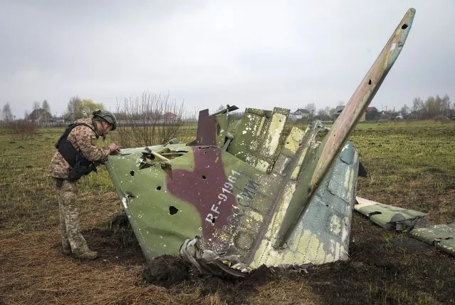 A Ukrainian soldier examines a fragment of a Russian Air Force Su-25 jet after a recent battle at the village of Kolonshchyna, Ukraine, Thursday, April 21, 2022. (Photo by Efrem Lukatsky/AP Photo)