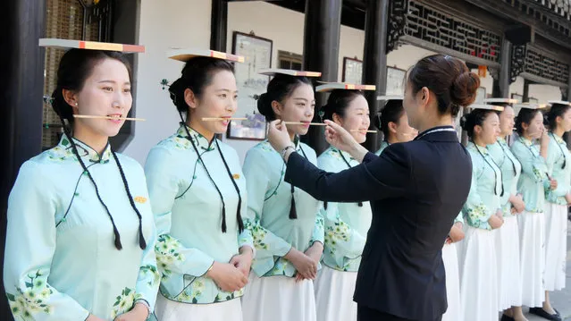 Tourist guides of Yangzhou Slender Lake Scenic Area balance books on their heads during an etiquette training class on May 18, 2017 in Yangzhou, Jiangsu Province of China. Tourist guides balance books on their heads with chopsticks in their mouths and poker in their hands under the guidance of a professional etiquette trainer. Tourist guides are trained to prepare for the upcoming China's National Tourism Day, which falls on May 19. (Photo by VCG/VCG via Getty Images)