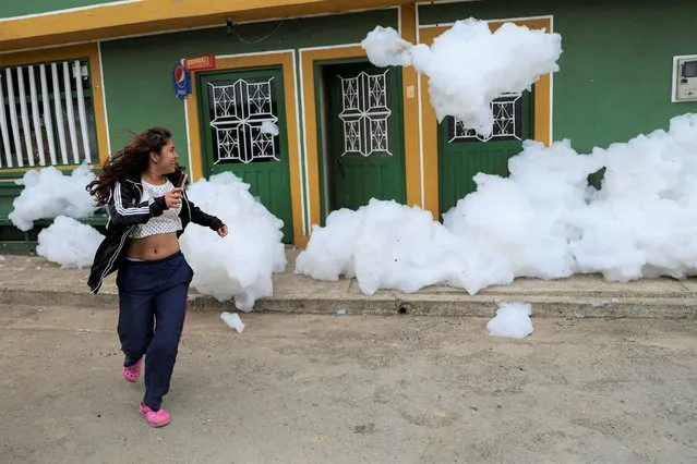 A woman flees from the polluting foam generated by a river full of waste, at the entrance of her house, in Mosquera, Colombia on April 27, 2022. (Photo by Luisa Gonzalez/Reuters)