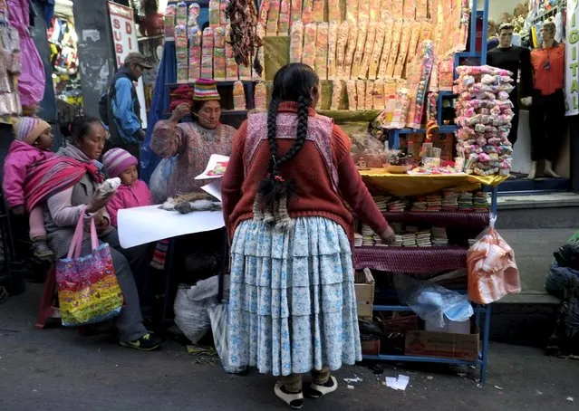 Aymara women are seen next to a stand with offering products at the witch doctor's street in La Paz, Bolivia July 31, 2015. (Photo by David Mercado/Reuters)