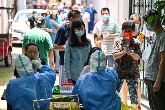 A health worker takes a swab sample from a woman at the entrance of a residential area under Covid-19 lockdown in the Changning district of Shanghai on June 11, 2022. (Photo by Hector Retamal/AFP Photo)