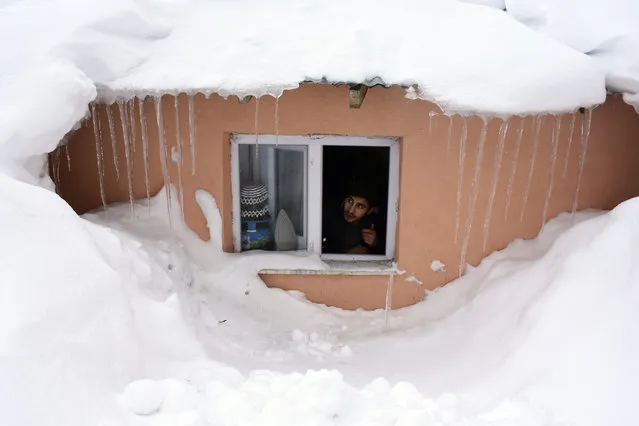 A man looks through a window of a house covered in snow, in Turkey's eastern Mus province on February 04, 2020. Heavy snow in Mus affect life in rural areas negatively. (Photo by Ibrahim Yaldiz/Anadolu Agency via Getty Images)