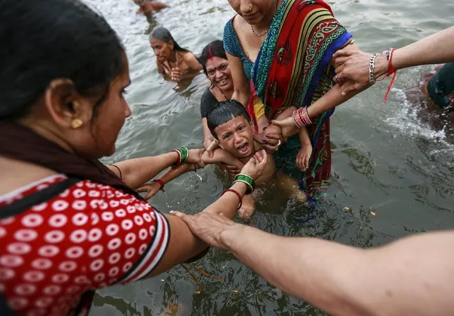 A boy cries as he is dipped by his relatives in the Godavari river during Kumbh Mela or the Pitcher Festival in Nashik, India, August 28, 2015. Hundreds of thousands of Hindus took part in the religious gathering at the banks of the Godavari river in Nashik city at the festival, which is held every 12 years in different Indian cities. (Photo by Danish Siddiqui/Reuters)