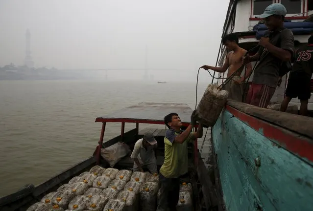 Workers transfer a container of cooking oil into wooden boat as haze shrouds the Batanghari River in Jambi, Indonesia Sumatra island, September 14, 2015. (Photo by Reuters/Beawiharta)