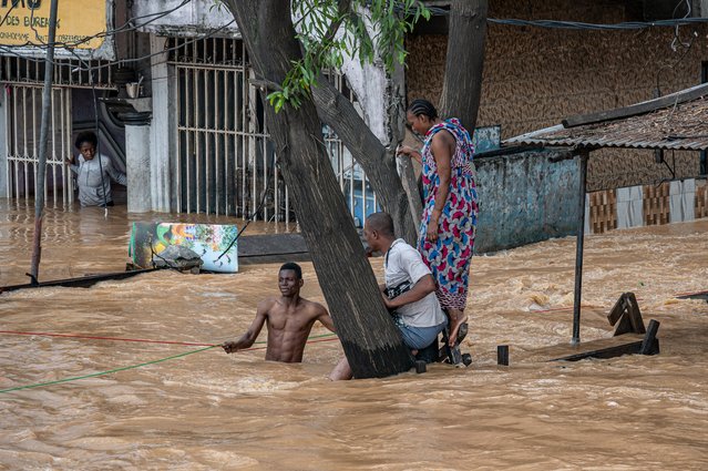 Residents stand on a tree for safety as floodwaters cover a road following heavy rains in the Ndjili district of Kinshasa on April 6, 2025. (Photo by Hardy Bope/AFP Photo)