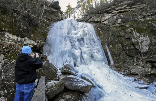 Bill Abee of Morganton, N.C., photographs a frozen over High Shoals Falls at South Mountains State Park on Friday, January 5, 2018 in Connelly Springs, N.C. The 60 foot waterfall is frozen over as a result of below freezing temperatures. (Photo by Kathy Kmonicek/AP Photo)