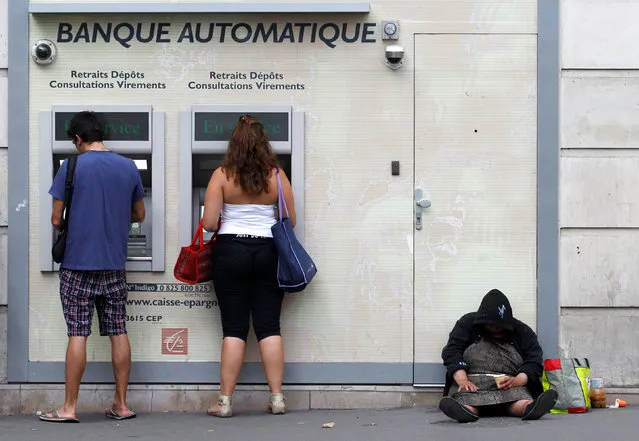 An homeless woman sits on a footpath while people withdraw money from ATMs along a main road in central Paris August  22, 2011. (Photo by Yves Herman/Reuters)