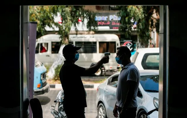 A Palestinian man takes the temperature of another man outside a supermarket in Gaza City on September 19, 2020, after the easing of restrictions due to the COVID-19 pandemic. (Photo by Mahmud Hams/AFP Photo)
