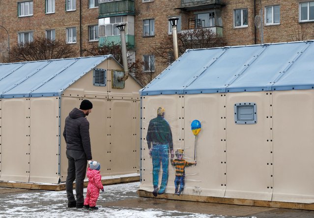 A man with a child looks an artwork of the famous street artist Tvboy, created on a wall of an 'invincibility centre', amid Russia's attack on Ukraine, in the town of Bucha, outside Kyiv, Ukraine on January 29, 2023. (Photo by Valentyn Ogirenko/Reuters)
