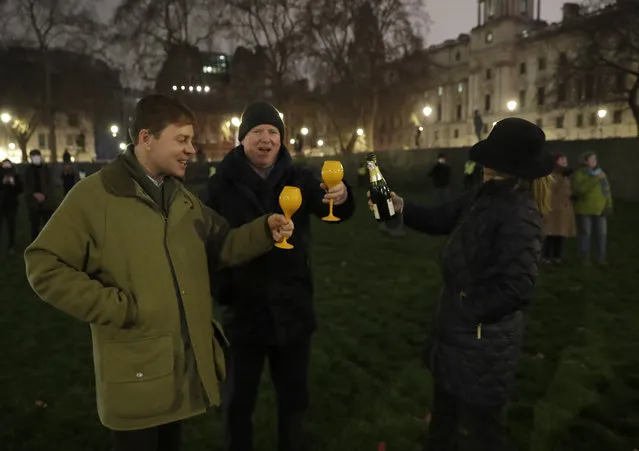 People raise a glass and celebrate in Parliament Square as the bell known as Big Ben strikes 2300, and Britain ends its transition period and formally leaves the European Union in London, Thursday, December 31, 2020. Due to the coronavirus pandemic and the restrictions on gatherings people were moved on by police if they met in any number. (Photo by Matt Dunham/AP Photo)