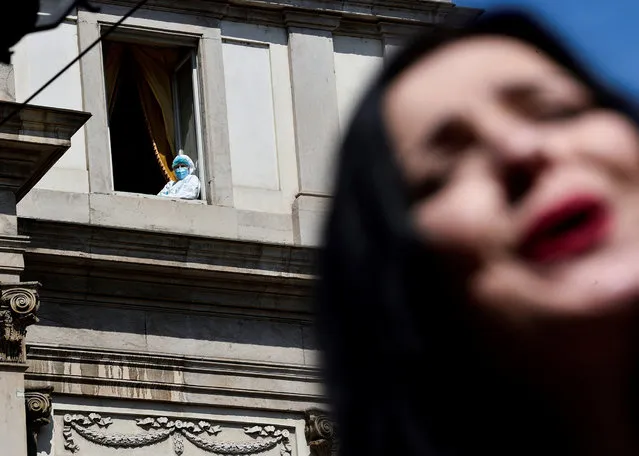 A person wearing a protective suit looks out from a window as opera singer performs the first act of Giacomo Puccini's famed romance opera “La Boheme” outside the La Scala theatre as part of a protest against the entertainment sector's crisis caused by the coronavirus disease (COVID-19) pandemic and restrictions, in Milan, Italy on April 20, 2021. (Photo by Flavio Lo Scalzo/Reuters)