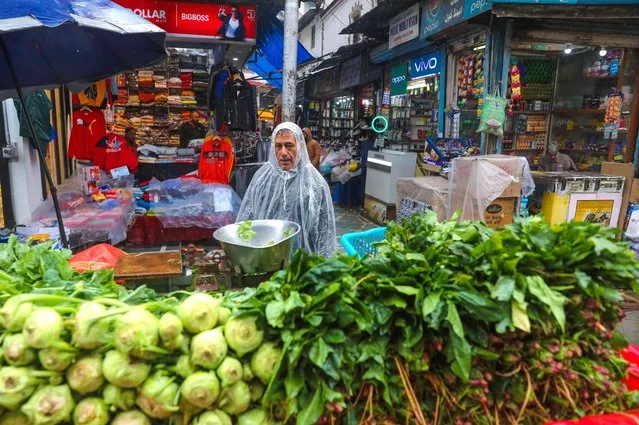 A vegetable vendor covers himself with polythene sheet as he waits for customers during rain in Srinagar, the summer capital of Indian Kashmir, India, 16 October 2023. The local Meteorological Department said that rain lashed plains and light snowfall occurred at higher reaches of Kashmir. (Photo by Farooq Khan/EPA)