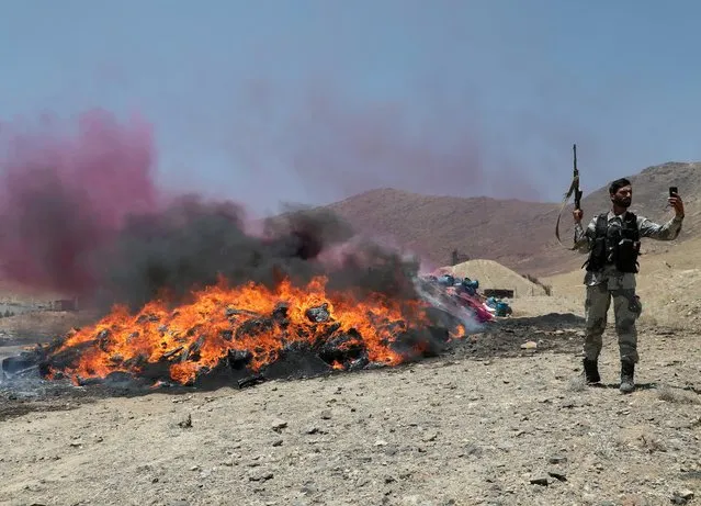 An Afghan police officer takes a selfie in front of a pile of burning illegal drugs on the outskirts of Kabul, Afghanistan July 1, 2021. (Photo by Omar Sobhani/Reuters)