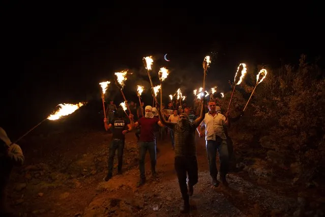 Palestinian demonstrators march with torches during a demonstration against the West Bank Jewish settlement outpost of Eviatar that was rapidly established last month, at the Palestinian village of Beita, near the West Bank city of Nablus, Saturday, June 26, 2021. The Palestinians say it was established on their farmland and fear it will grow and merge with other large settlements in the area. (Photo by Majdi Mohammed/AP Photo)
