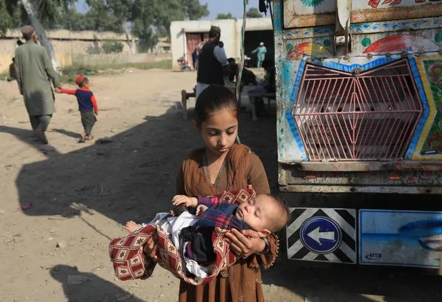 An Afghan girl carries her seven month-old sister Haleema, as her family returns home, after Pakistan gives last warning to undocumented immigrants to leave, outside the United Nations High Commissioner for Refugees (UNHCR) repatriation centres in Azakhel town in Nowshera, Pakistan on November 3, 2023. (Photo by Fayaz Aziz/Reuters)