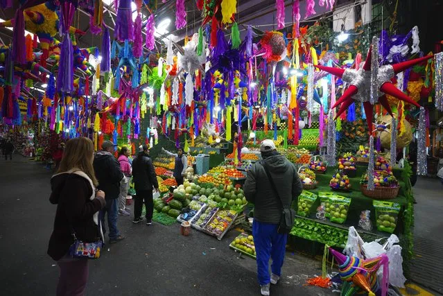 Christmas piñatas for sale hang over a fruit vendor's stall at the Jamaica market in Mexico City, December 14, 2023. The breaking open of piñatas are part of the Mexican Christmas tradition. (Photo by Fernando Llano/AP Photo)