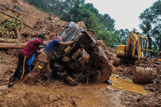 Rescue workers push a overturned vehicle stuck in the mud and debris at a site of a landslide claimed to be caused by heavy rains in Kokkayar in India's Kerala state on October 17, 2021. (Photo by AFP Photo/Stringer)