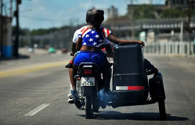 A woman wearing a t-shirt in the colours of the US flag rides a motorcycle in Havana on March 17, 2016. Hundreds of workers have been scrambling for days to touch up building facades, patch potholes and spiff up Havana's monuments ahead of US President Barack Obama's visit. Obama next week will become the first US president to visit Cuba while in office in almost a century. (Photo by Yamil Lage/AFP Photo)