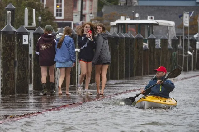 A group of people walk on the sea wall as a man kayaks through the flooded parking lot in downtown Annapolis, Maryland, on October 29, 2021. The US National Weather Service implemented a flood watch for the cities of Baltimore and Annapolis as well as Anne Arundel, Baltimore and Howard counties. Washington, DC, and parts of Virginia faced the same alert. (Photo by Jim Watson/AFP Photo)