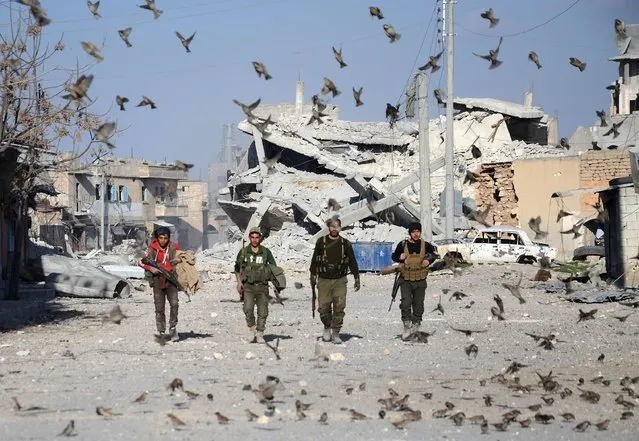 Birds fly in front of Turkish-backed Syrian rebels walking in the northwestern border town of al-Bab on February 23, 2017 after they fully captured the town from the Islamic State (IS) group. Al-Bab, just 25 kilometres (15 miles) south of the Turkish border, was the last IS stronghold in the northern Syrian province of Aleppo. (Photo by Nazeer al-Khatib/AFP Photo)
