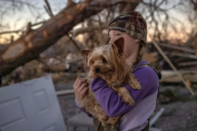 Braelyn Todd, 8, holds her dog Abner, a Yorkshire Terrier, as her parents help a family member clear debris from their destroyed home in the aftermath of a tornado in Mayfield, Kentucky, U.S. December 12, 2021. (Photo by Adrees Latif/Reuters)