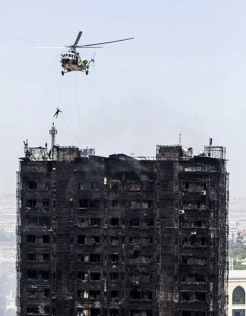 A rescuer descends from a helicopter over the roof of a burnt multi-storey residential building in Baku, Azerbaijan, May 19, 2015. (Photo by Ehtiram Jabi/Reuters)